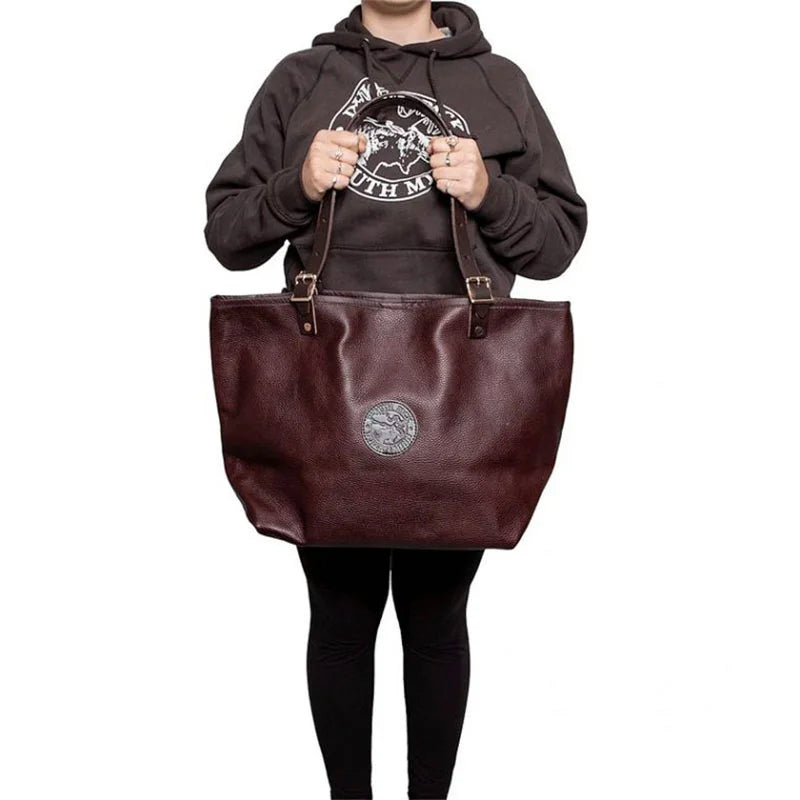 Leather Market Tote in rich brown USA leather with adjustable premium handles, held by a person wearing casual outdoor apparel, showcasing durable craftsmanship.