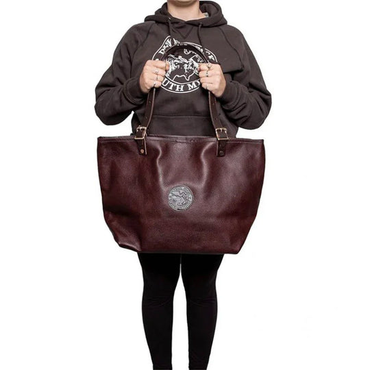 Leather Market Tote in rich brown USA leather with adjustable premium handles, held by a person wearing casual outdoor apparel, showcasing durable craftsmanship.