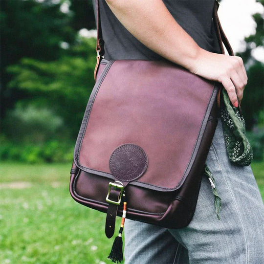 Leather Haversack in rich brown leather with premium buckle strap, worn outdoors by a person dressed casually, showcasing durable handcrafted design by Duluth Pack.