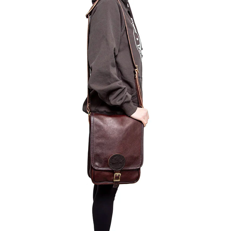 Leather Haversack in rich brown premium leather with buckle closure, worn crossbody by a person in casual outdoor clothing emphasizing durable outdoor gear.