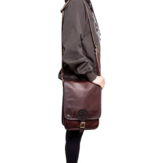 Leather Haversack in rich brown premium leather with buckle closure, worn crossbody by a person in casual outdoor clothing emphasizing durable outdoor gear.