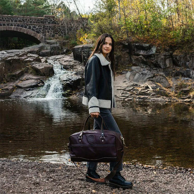 Leather Weekender Duffel held by Woman by River and Bridge