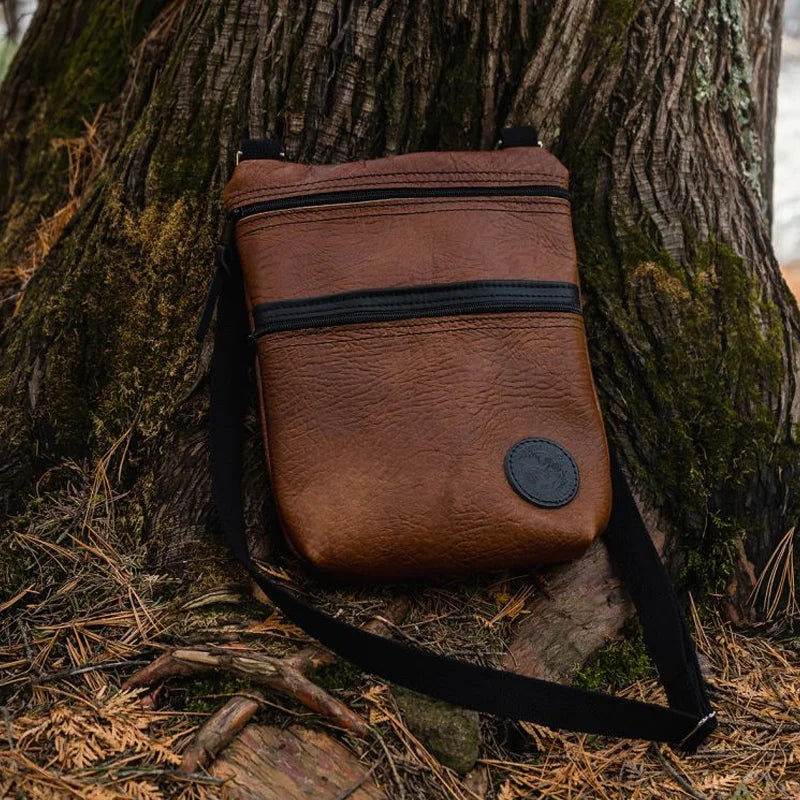 Bison Leather Traverse Crossbody Bag in front of a tree 