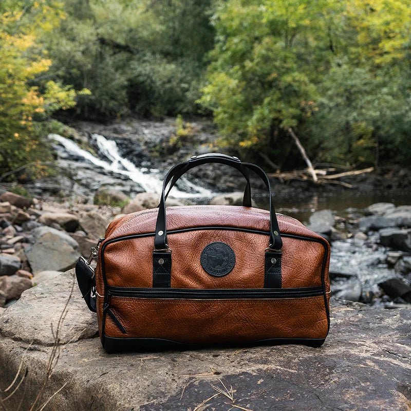 Duluth Pack Bison Leather Weekender Duffel in black in front of a creek
