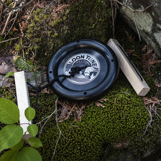 The LoonTune black circular outdoor toy by LOON TUNE placed on green moss with wooden handles, highlighting its rugged design and heritage quality craftsmanship.