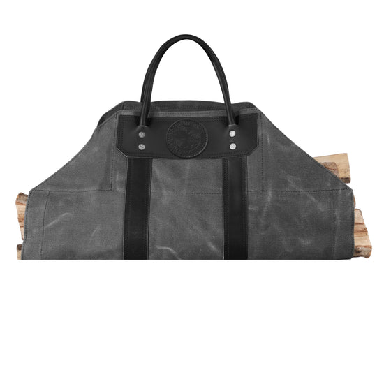Log Carrier in sturdy gray canvas with black leather reinforcements and handles, shown carrying firewood for outdoor and cabin use.
