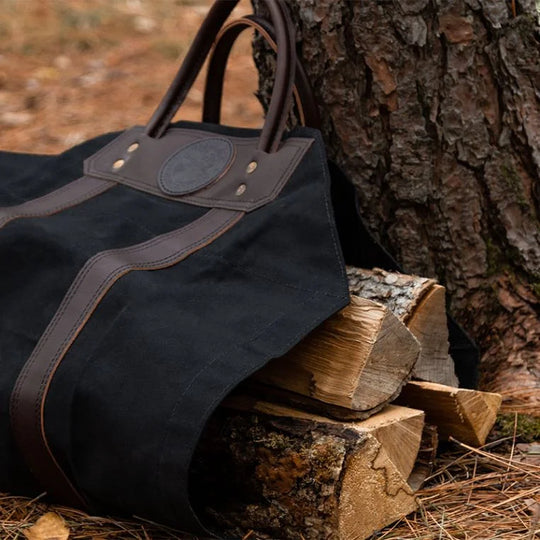 DOODLE BAG CHARM (PDP Test) featuring rugged black canvas and leather accents, placed outdoors on stacked firewood highlighting durable craftsmanship by DOUGLAS COMPANY, INC.
