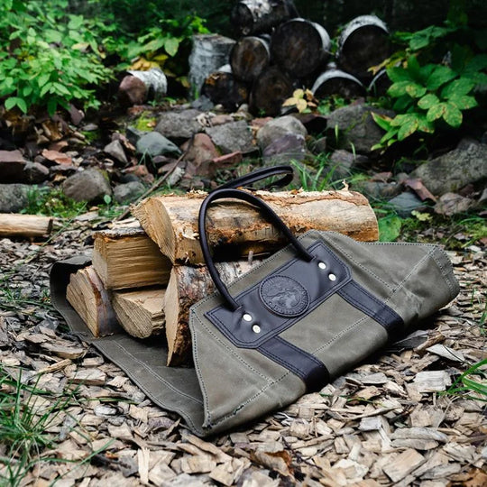Log Carrier with riveted leather reinforcements and durable canvas fabric, shown outdoors carrying firewood near a stacked woodpile, ideal for rugged use.