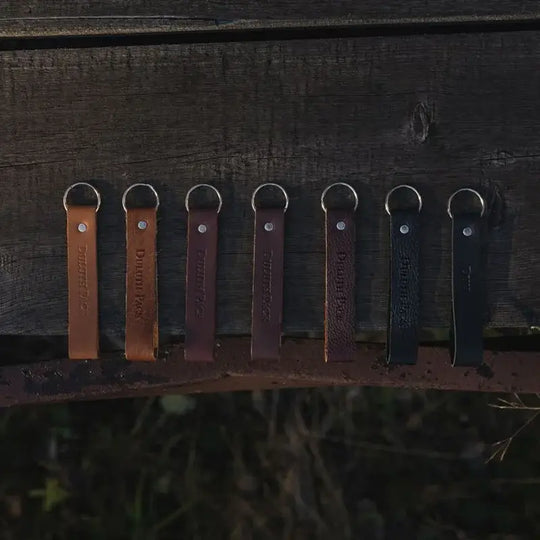 Duluth Pack Leather Keychain in tan, brown, black, peddled black, pebbled brown, and bison leather with dark wood background
