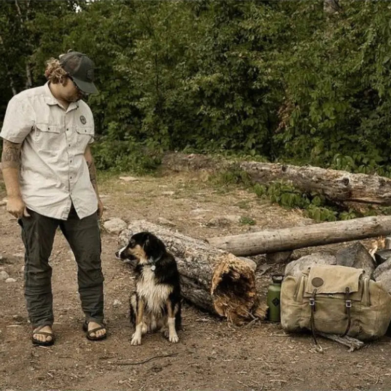 Duluth Pack Camp Kitchen Pack in waxed khaki in a camping setting with a man and dog