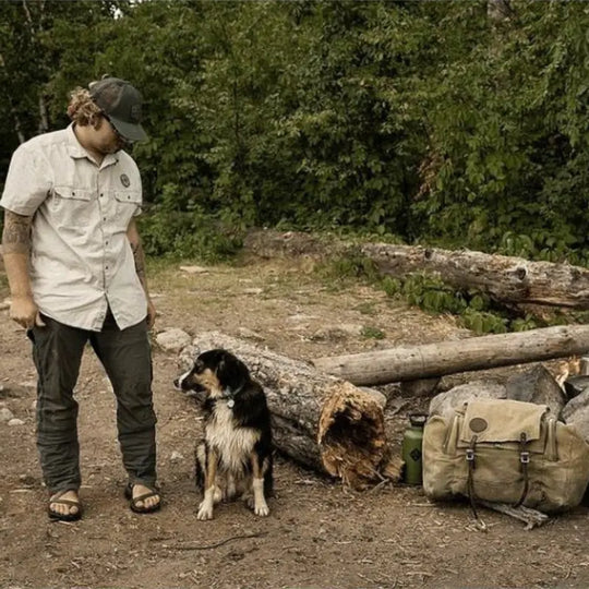 Duluth Pack Camp Kitchen Pack in waxed khaki in a camping setting with a man and dog
