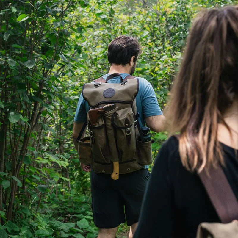 Outlander Pack in rugged canvas and leather, worn by a man hiking through dense green forest, showcasing durable outdoor gear handcrafted by Duluth Pack.