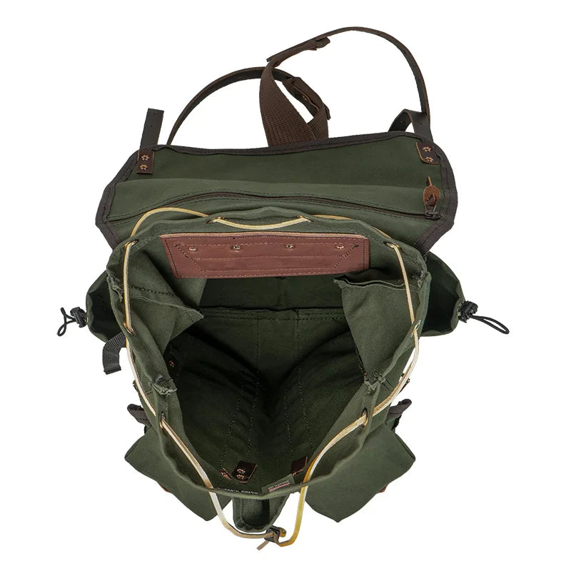Outlander Pack in olive green canvas with leather trim, handmade for rugged outdoor use by Duluth Pack, showing spacious interior and organized compartments on a trail setting.