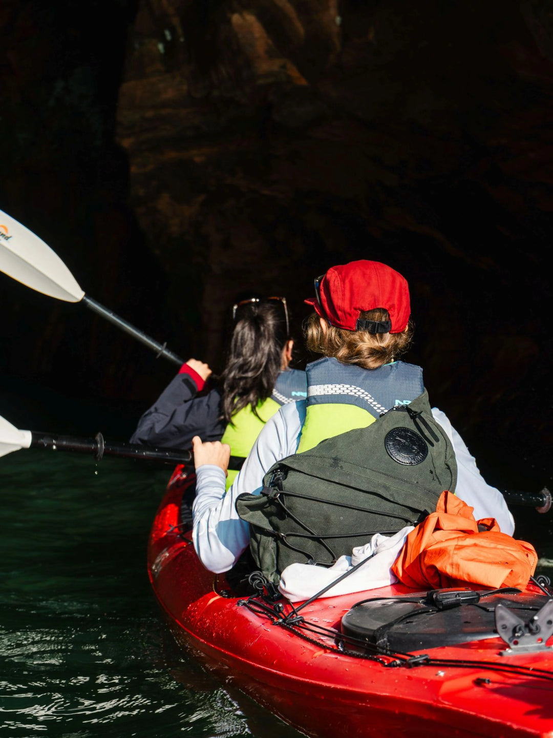 A woman in a sea kayak wearing a Duluth Pack Sling Pack with another girl  in the background.