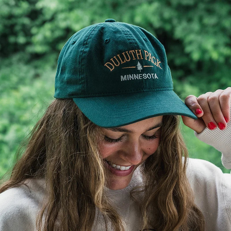 Duluth Pack Tree Scholar Hat in green with woman wearing the hat with forest background