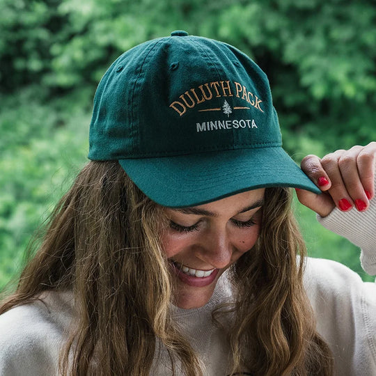 Duluth Pack Tree Scholar Hat in green with woman wearing the hat with forest background