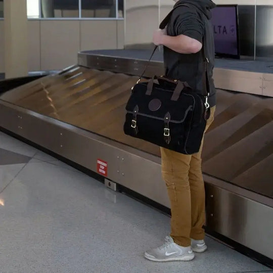 Classic Carry-On Bag In Black Being Carried By A Man Near A Baggage Carousel At An Airport