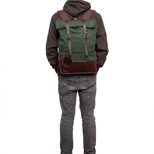 Deluxe Roll-Top Scout Pack in Olive Drab with brown leather accents worn by a person outdoors, showcasing durable handmade canvas backpack ideal for rugged use from Duluth Pack.