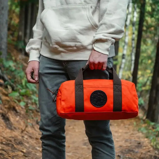 Utility Bag In Orange Being Held By A Man On A Trail Through The Woods